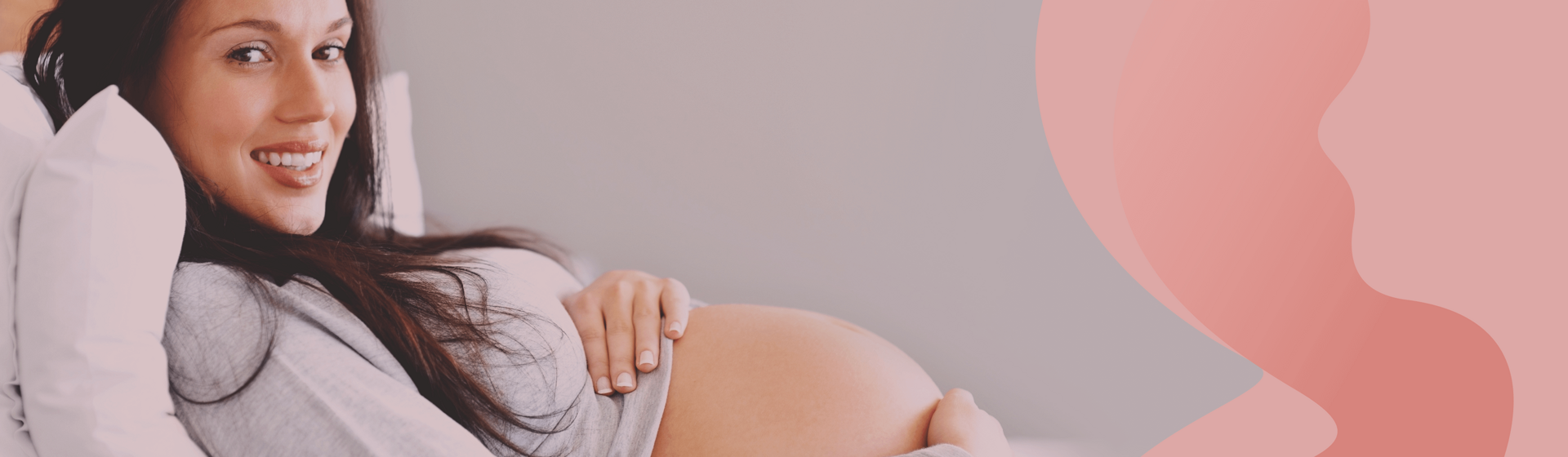 Pregnant woman reclined on her bed wtih some pillows, looking and smiling at the camera.