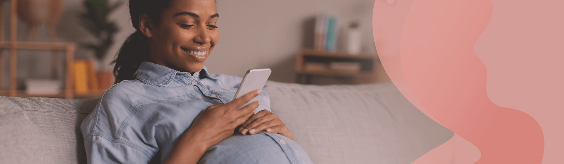 Pregnant woman sitting on a couch, looking at her smarphone and smiling.